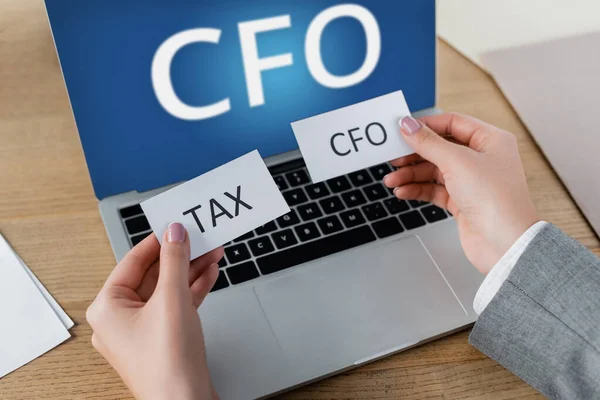 Cropped view of woman holding papers with lettering near laptop with cfo on screen — Stock Photo