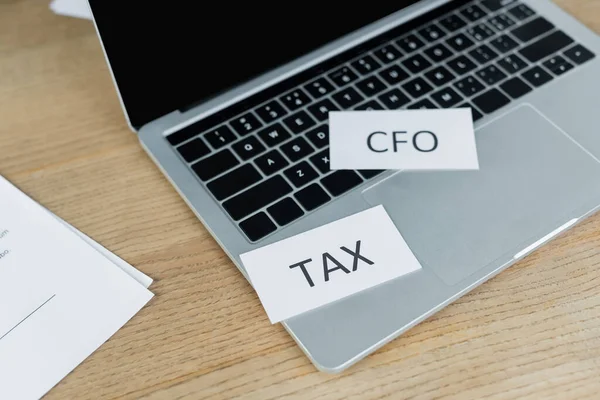 Papéis com imposto e cfo lettering perto de laptop com tela em branco — Fotografia de Stock