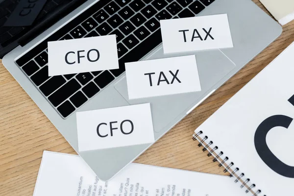 Top view of papers with tax and cfo lettering on laptop near notebook on desk — Stock Photo