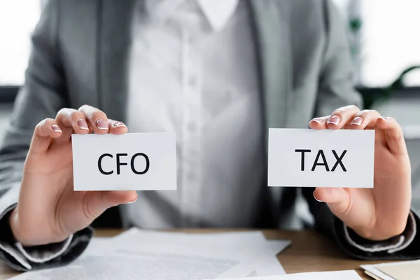 Cropped view of woman holding papers with cfo and tax lettering in office — Stock Photo