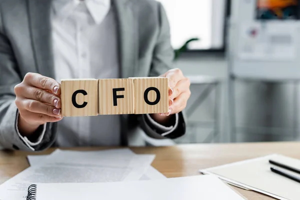 Vista ritagliata di donna d'affari che tiene cubi di legno con iscrizione cfo in ufficio — Foto stock