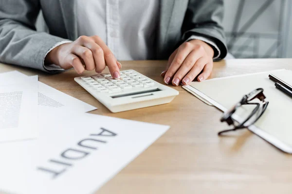 Visão parcial do inspetor fiscal usando calculadora perto de papel com letras de auditoria — Fotografia de Stock