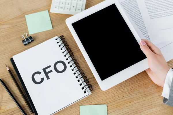 Top view of woman holding digital tablet with blank screen near notebook with cfo lettering and stationery — Stock Photo