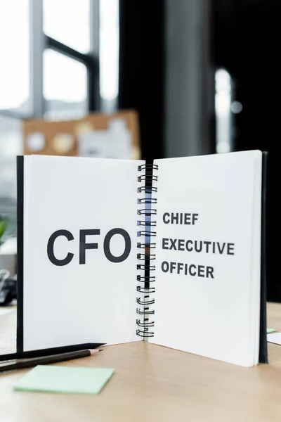 Cuaderno con cfo y el director ejecutivo de letras cerca de lápices en la mesa - foto de stock