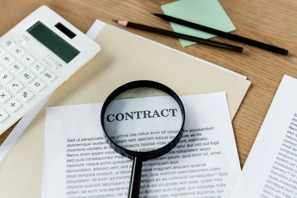 Magnifier on papers with contract lettering near calculator and documents — Stock Photo