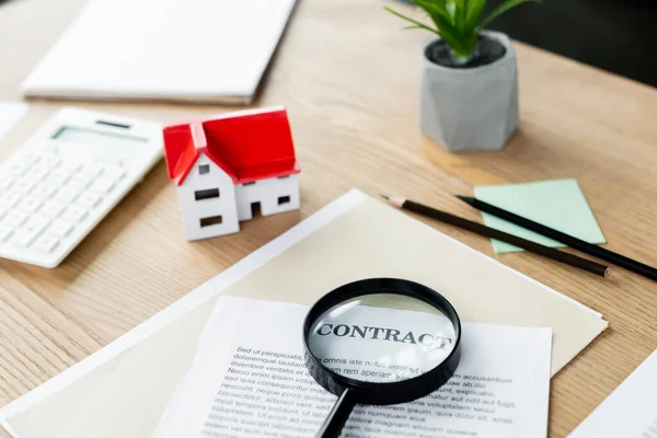 Lupa no contrato perto do modelo da casa da caixa perto da calculadora na mesa — Fotografia de Stock