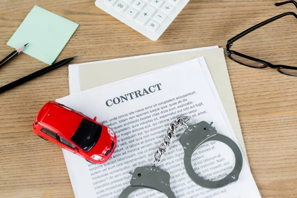 Blick von oben auf Spielzeugauto auf Vertrag in der Nähe von Handschellen und Brille auf dem Schreibtisch — Stockfoto