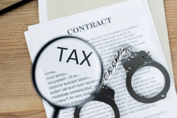 Top view of magnifier above document with tax and contract lettering near handcuffs — Stock Photo