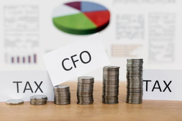 Stacked silver coins near papers with tax and cfo lettering near blurred charts — Stock Photo