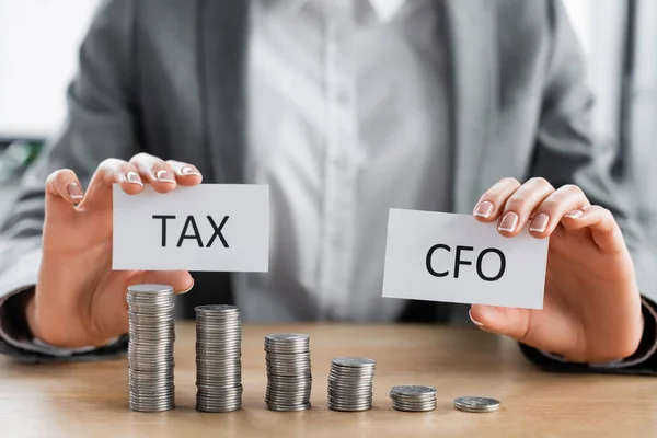 Cropped view of woman holding papers with tac and cfo lettering near stacked silver coins on table — Stock Photo