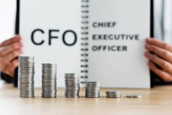Monete d'argento accatastate vicino sfocato ispettore fiscale che detiene notebook con cfo e lettering amministratore delegato — Foto stock