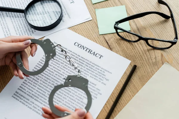 Ausschnitt eines Steuerinspektors mit Handschellen in der Nähe von Lupe und Dokumenten auf dem Schreibtisch — Stockfoto