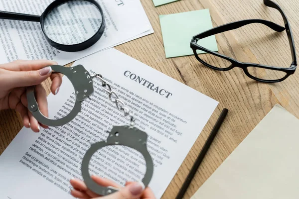 Cropped view of tax inspector holding handcuffs near magnifier and documents on desk — Stock Photo