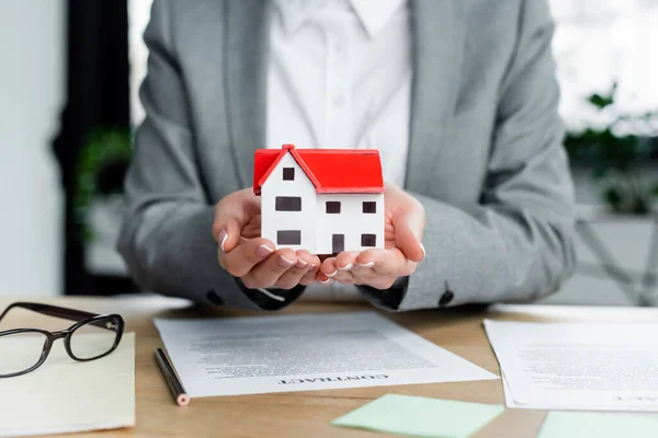 Cropped view of tax inspector holding house model near documents on desk — Stock Photo