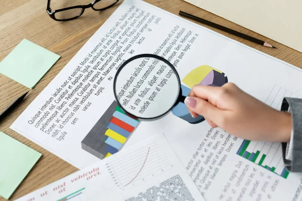 Cropped view of chief financial officer holding magnifier above charts on desk — Stock Photo