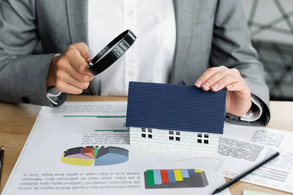 Ausgeschnittene Ansicht des Steuerinspektors mit Lupe über dem Hausmodell in der Nähe von Diagrammen auf dem Tisch — Stockfoto