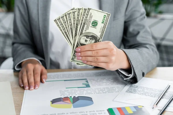 Vista recortada de la mujer de negocios sosteniendo billetes de dólar cerca de gráficos en la tabla - foto de stock