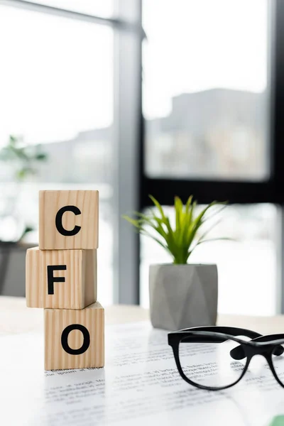 Würfel mit cfo-Buchstaben in der Nähe von Gläsern und Dokumenten auf dem Schreibtisch — Stockfoto