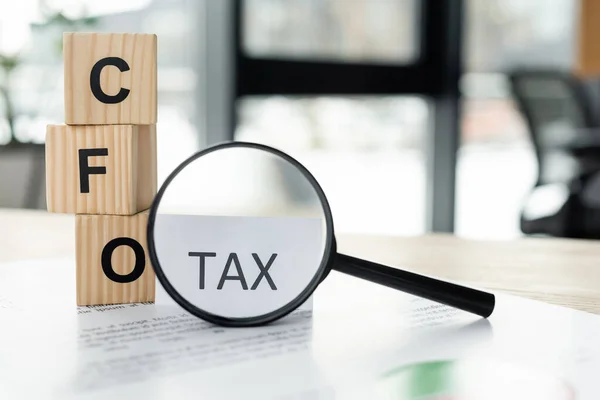 Magnifying glass near cubes with cfo letters and document with tax word on desk — Stock Photo