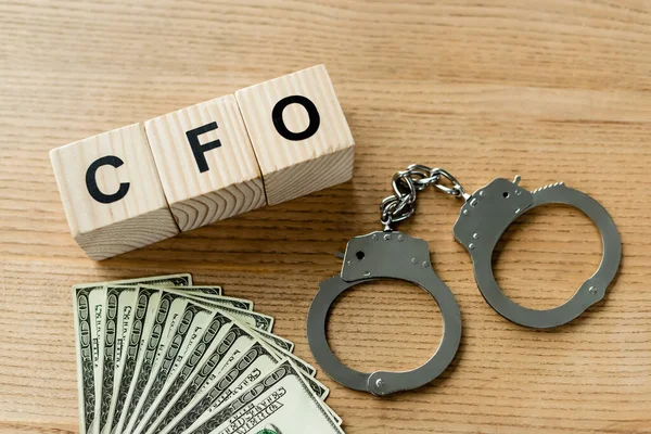 Top view of wooden cubes with cfo letters near handcuffs and money on desk — Stock Photo