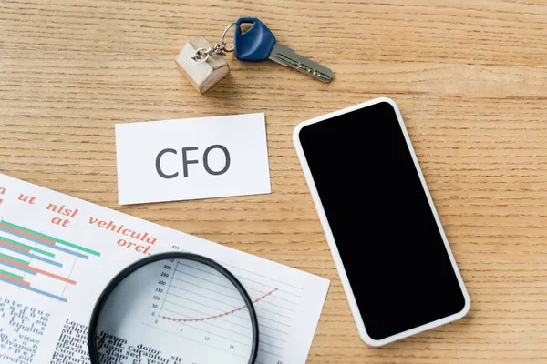 Top view of magnifier near charts, paper with cfo lettering near smartphone with blank screen — Stock Photo