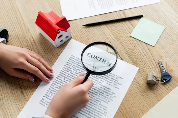 Cropped view of tax inspector holding magnifier above contract and house model on desk — Stock Photo