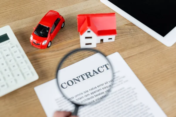 Top view of tax inspector holding magnifier above contract near house model and toy car — Stock Photo