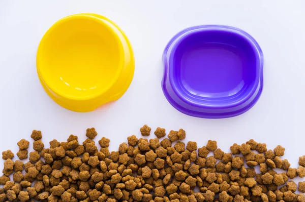 Vista superior de tigelas de plástico amarelo e roxo perto de alimentos para animais de estimação isolados em branco — Fotografia de Stock