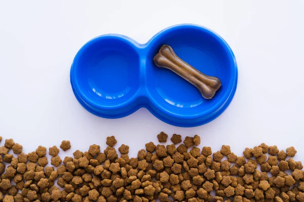 Top view of bone shaped dog treat in blue bowl near pet food — Stock Photo