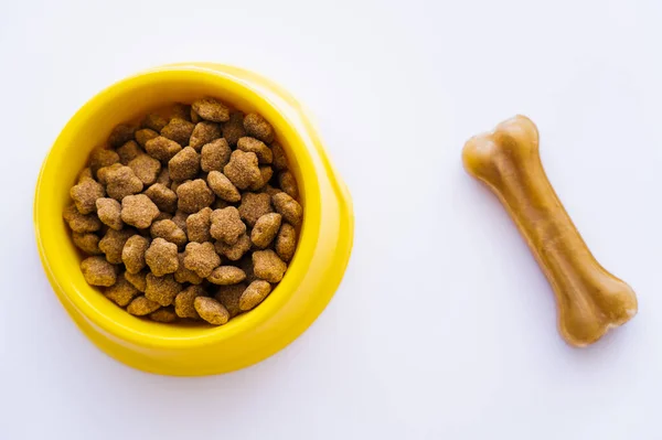Vista superior del recipiente de plástico amarillo con comida para mascotas cerca del perro tratar aislado en blanco - foto de stock