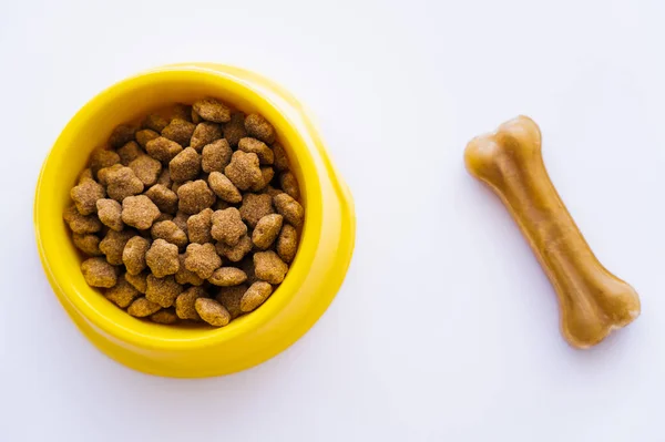 Vue du dessus du bol en plastique jaune avec nourriture pour animaux de compagnie près de gâterie pour chien isolé sur blanc — Photo de stock