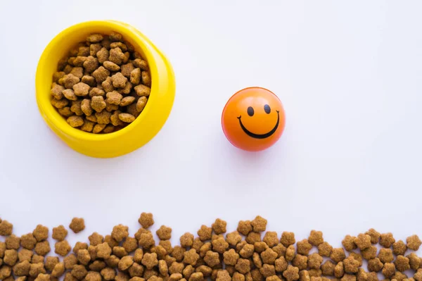 Top view of ball with smiley emoticon near pet food in bowl isolated on white — Stock Photo