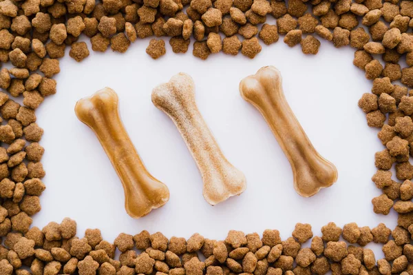 Disposición plana de las golosinas en forma de hueso en el marco con alimentos para mascotas secos aislados en blanco - foto de stock