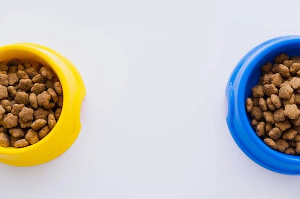 Vista superior de tigelas azuis e amarelas com alimentos para animais de estimação isolados em branco — Fotografia de Stock
