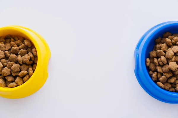 Top view of blue and yellow bowls with pet food isolated on white — Stock Photo