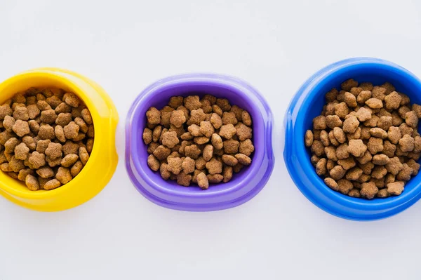 Vista superior de tigelas coloridas com alimentos secos para animais de estimação isolados em branco — Fotografia de Stock