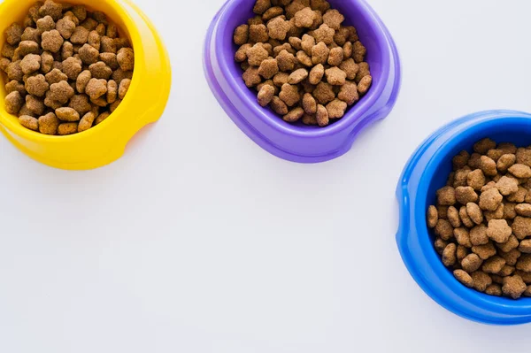 Vue de dessus des bols colorés avec différents aliments pour animaux isolés sur blanc — Photo de stock