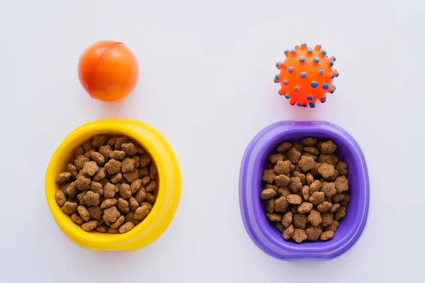 Top view of rubber toys near bowls with pet food on white — Stock Photo