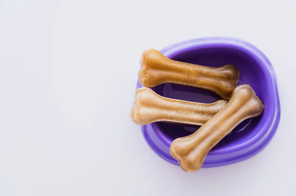 Vue de dessus des friandises pour animaux en forme d'os dans un bol violet isolé sur blanc — Photo de stock