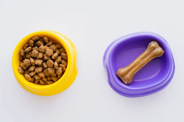 Vista superior de ossos em forma de animais de estimação trata em tigela perto de alimentos secos para animais de estimação isolados em branco — Fotografia de Stock