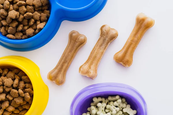 Vista da vicino di ossatura tratta animale domestico vicino ciotole con cibo animale domestico secco e biscotti isolati su bianco — Foto stock