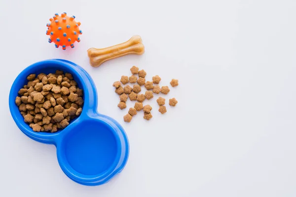 Vista superior de la mascota en forma de hueso tratar cerca de cuenco con comida seca para mascotas y juguete de goma aislado en blanco - foto de stock