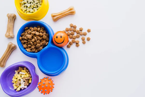 Vista superior de guloseimas em forma de osso perto de tigelas com alimentos secos para animais de estimação e brinquedos de borracha isolados em branco — Fotografia de Stock