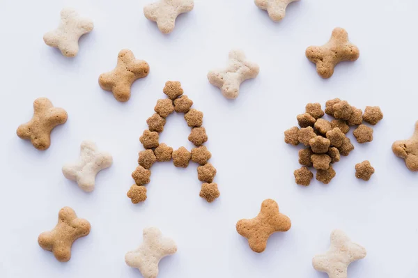 Top view of bone shaped pet treats near letter and dry pet food isolated on white — Stock Photo