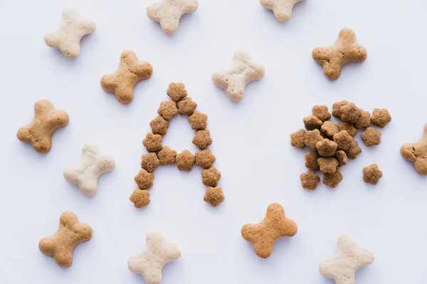 Vista superior de ossos em forma de animais de estimação trata perto da letra e alimentos secos para animais de estimação isolados em branco — Fotografia de Stock