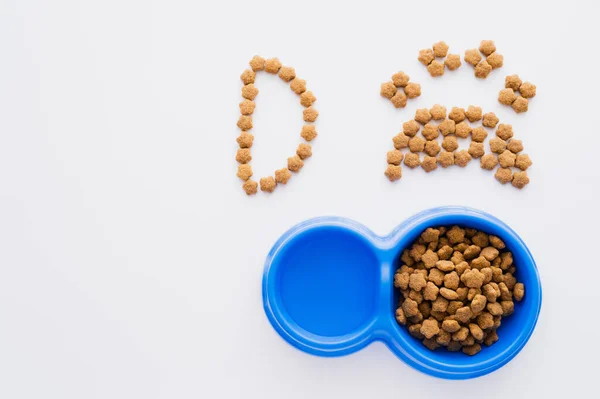 Vista dall'alto della forma della zampa fatta di cibo per animali domestici asciutto vicino lettera e ciotole isolate su bianco — Foto stock