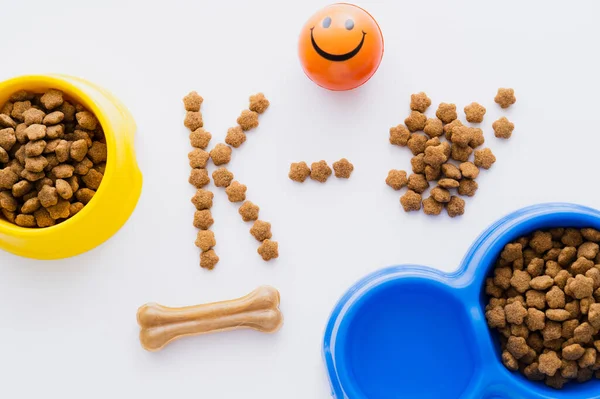 Vista dall'alto di cibo per animali domestici asciutto vicino a ciotole e palla di gomma isolata su bianco — Foto stock