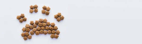 Vue de dessus de la forme de patte en nourriture sèche pour animaux isolés sur blanc, bannière — Photo de stock