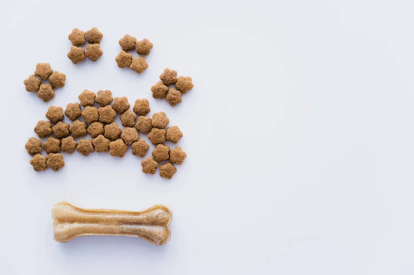 Vista superior da forma da pata feita de alimento seco para animais de estimação perto do osso isolado no branco — Fotografia de Stock