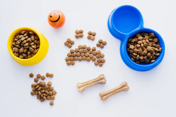 Vista dall'alto della forma della zampa fatta di cibo per animali domestici asciutto vicino a ossa e ciotole isolate su bianco — Foto stock